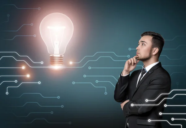 Young man in business suit thinking about idea, on concrete wall background. Shining light bulb. Business concept — ストック写真