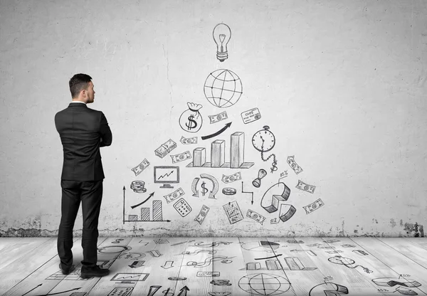 Young businessman in suit, standing front of concrete wall with business sketches on it. — ストック写真