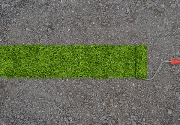 Strip of green grass made by roller for painting on a ground with small stones. — Stock Photo, Image