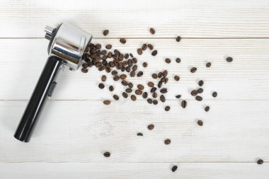 Üst görünümde ahşap yüzeyüzerinde dağınık kahve çekirdekleri ile Portafilter kolu