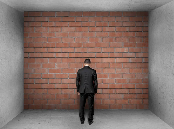 Бизнесмен со склоненной головой стоит перед кирпичной стеной в интерьере . — стоковое фото