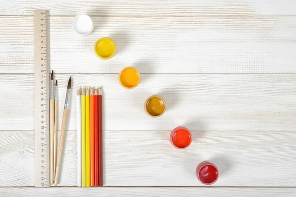 Vista dall'alto di pennelli e matite con contenitori di guazzo colorati su sfondo di legno . — Foto Stock