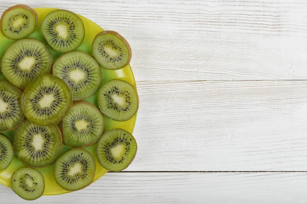 Dish full of kiwi slices on wooden surface with copy space.