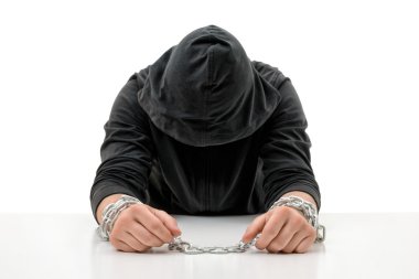 Elleri zincirli adam baş eğdi oturuyor.