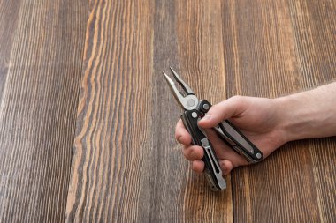 Yakın çekim yakışıklı bir ahşap arka plan üzerinde multitool tutan adamın