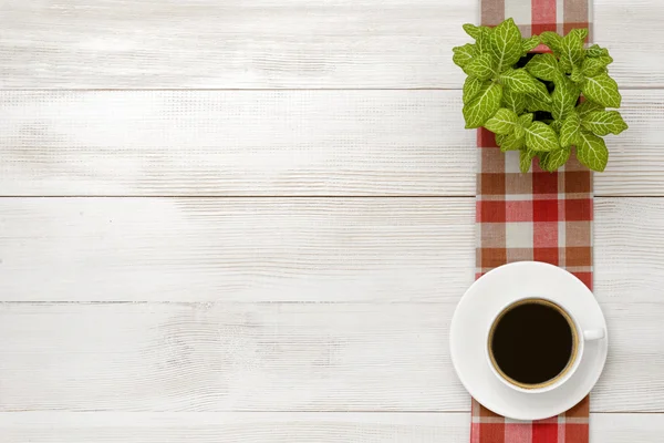 Kantoor werkplek met groene kamerplant op geruit tafelkleed, kopje koffie — Stockfoto