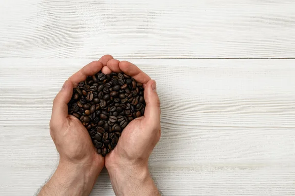 Close-up mãos de homem segurando um punhado de grãos de café com espaço de cópia — Fotografia de Stock