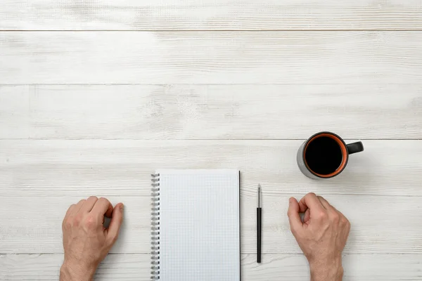 Handen van man met potlood, notitieboekje en kopje koffie, staande op de houten tafel — Stockfoto