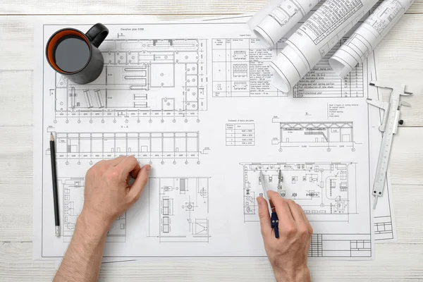 Mãos de perto do homem segurando um divisor de engenharia sobre o plano de desenho na vista superior — Fotografia de Stock