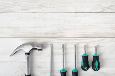 Açık alana sahip ahşap yüzeyde çekiç ve farklı boy tornavidalar dahil olmak üzere inşaat araçlarının üst görünümü.