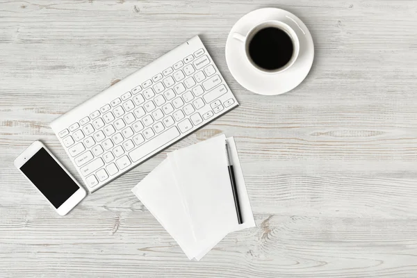 Pracoviště s šálkem kávy, klávesnice, smarthphone, bílé listy a pera na dřevěné desce v pohledu shora. — Stock fotografie