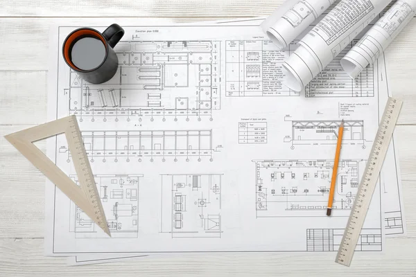 Rolls of drawing sketches, magnifier, ruler and protractor are on wooden surface.