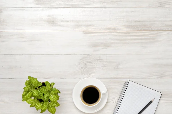 Pracoviště s šálkem kávy, pokojové rostliny, prázdný zápisník a tužku na dřevěné desce — Stock fotografie