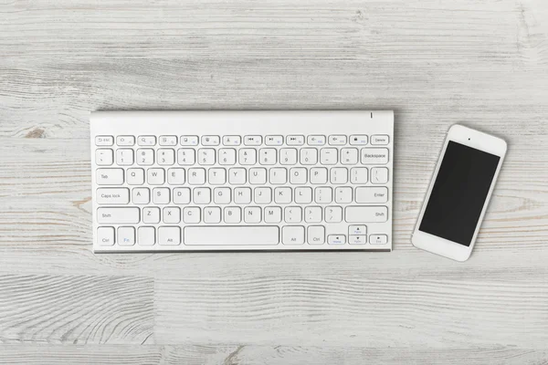 Bovenaanzicht van werkplek met toetsenbord en smartphone op houten tafel — Stockfoto