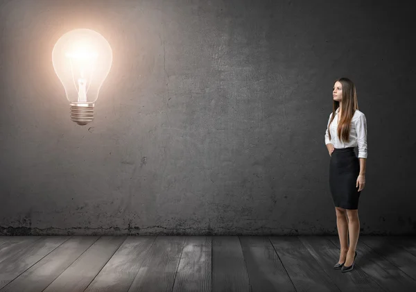 Jovem empresária de pé e olhando para grande lâmpada brilhante na frente dela — Fotografia de Stock