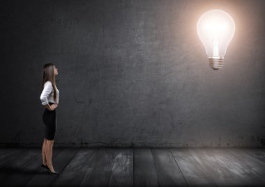 Ayakta ve onun önünde büyük parlayan ampul bakarak genç iş kadını