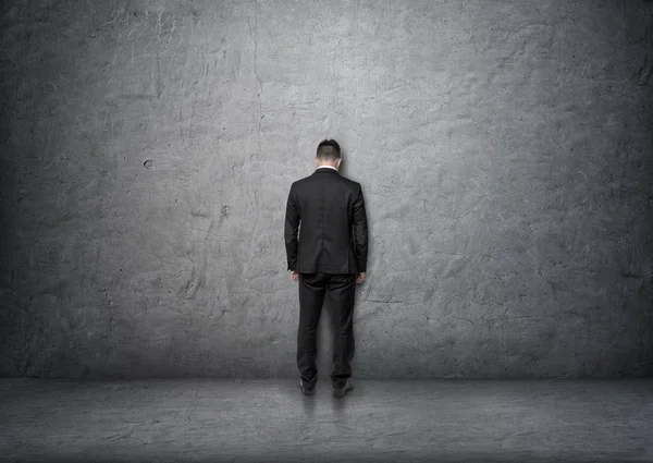 Back View affärsman med böjt huvud stående framför betongväggen — Stockfoto