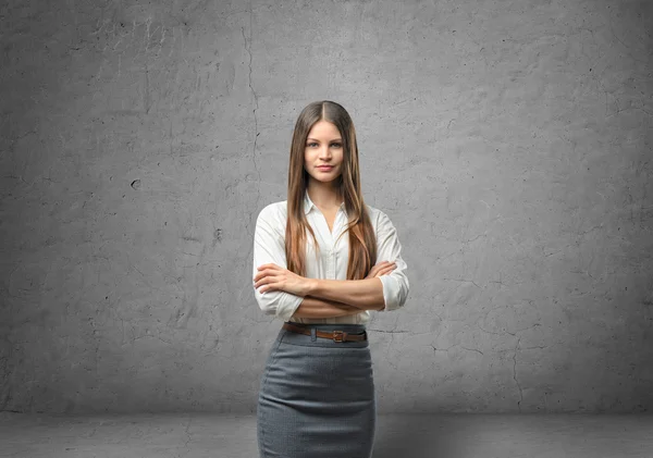 Young businesswoman with her arms folded in the background of concrete wall — Stockfoto