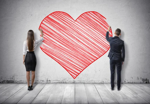 Homme d'affaires et femme d'affaires dessinant un grand cœur rouge sur un mur en béton — Photo