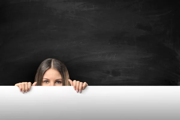 Woman peeking over the edge of blank empty paper billboard with copy space — Stockfoto