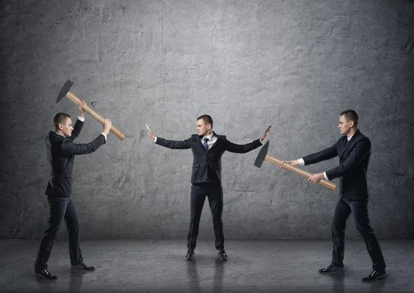 Businessman separating two fighting businessmen with hammers