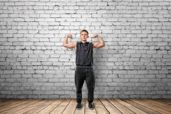 Gespierde jongeman zijn biceps spieren te tonen op de achtergrond van witte bakstenen muur — Stockfoto