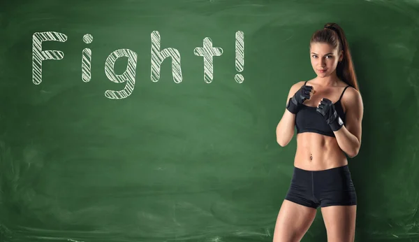 Fitness girl clenching her fists ready to fight on the background of a chalkboard — Stock Photo, Image