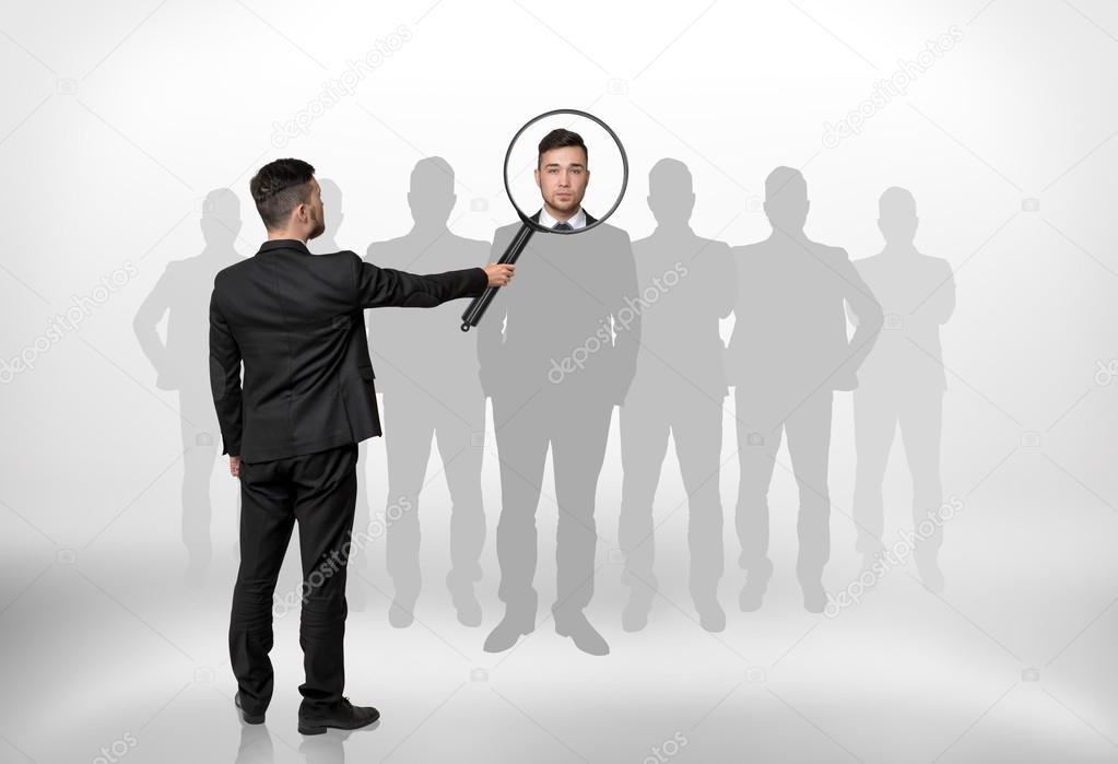 Businessman looking through magnifying glass on the head of the man that is surrounded by grey silhouettes