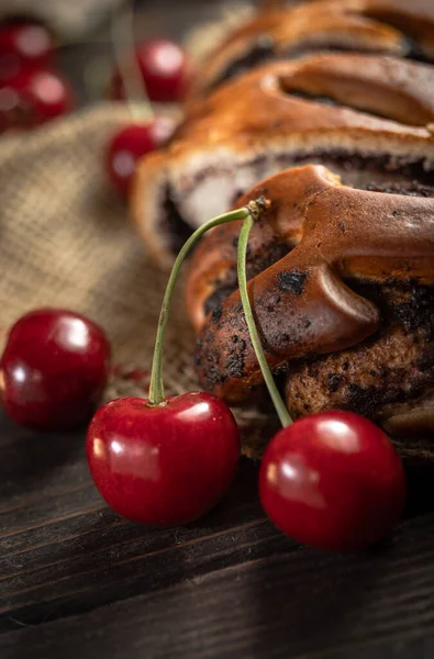 Bun with poppy seeds and fresh cherries on a wooden background