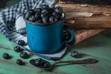 Kırsal arka planda yabanmersinli mavi vintage demir bardak.
