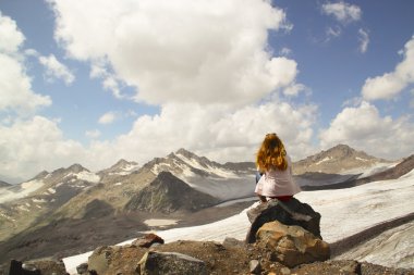 bir uçurumun kenarında oturan ve gökyüzüne bakarak genç kız