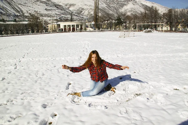 Gelukkig jong meisje, zittend op de sneeuw in het park op een zonnige wint — Stockfoto