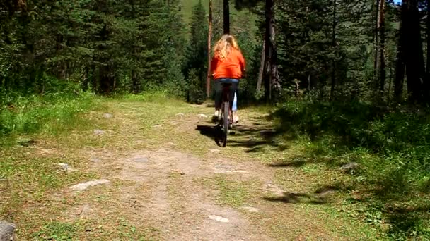 Chica joven montando una bicicleta en el bosque en un camino de tierra — Vídeo de stock