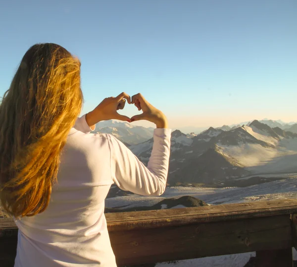 Silhouette girl making a heart shape with her hands, greeting an