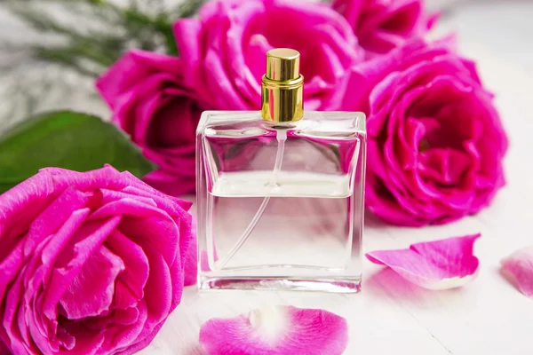 Perfume de rosas em garrafa transparente com rosas e pétalas rosa — Fotografia de Stock