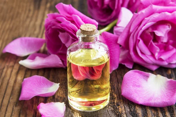 Aceite esencial de rosa con rosas rosadas y pétalos sobre tabla de madera —  Fotos de Stock