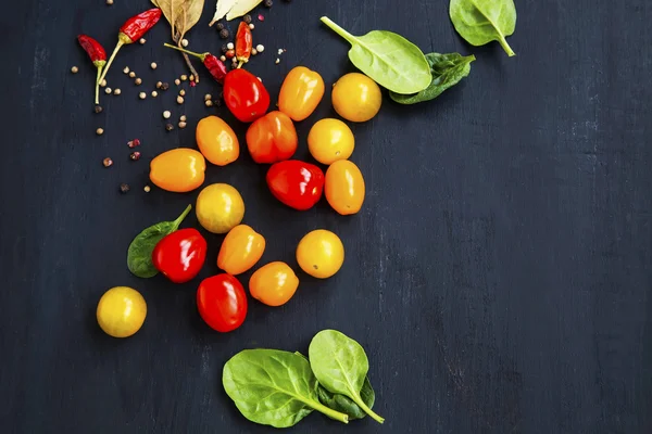 Organické žluté a červené cherry rajčata s listovým špenátem a koření — Stock fotografie