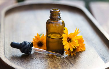 Pipetli Calendula yağı şişesi ve ahşap tepside çiçek.