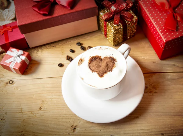 Herzförmige Cappuccino-Tasse mit Schlagsahne und verpackten Geschenken — Stockfoto