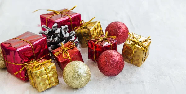 Goldene und rote Weihnachtsgeschenke und Kugeln im Schnee — Stockfoto
