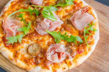 Yakın plan pizza, ahşap pizza tahtasında taze roka ile süslenmiş. Parlak taş arkaplanı