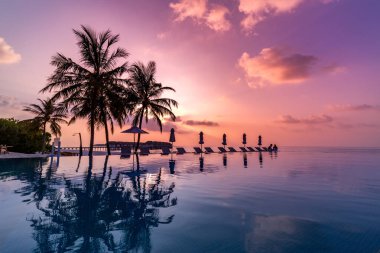 Amazing mood with poolside and palms next to beach and the ocean. Sunset sky and calm sea for luxury vacation tourism concept. Infinity swimming pool under colorful sky. Travel tourism destination, relaxing vibes