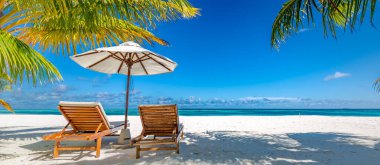 Beautiful tropical scenery, two sun beds, loungers, umbrella under palm tree. White sand, sea view with horizon, clear blue sky, calmness and relaxation. Inspirational beach resort hotel. Luxury island resort vacation or holiday