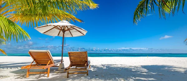 Beautiful tropical scenery, two sun beds, loungers, umbrella under palm tree. White sand, sea view with horizon, clear blue sky, calmness and relaxation. Inspirational beach resort hotel. Luxury island resort vacation or holiday