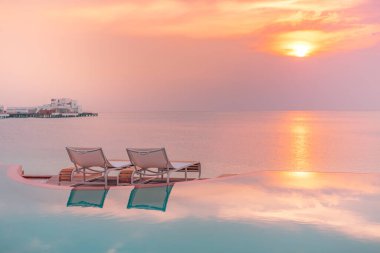 Romantik sahil gün batımı, plaja bakan lüks bir otelde sonsuz bir yüzme havuzu gün batımında mükemmel plaj tatili afişi. Gün batımı plaj manzarası. Birkaç dinlenme yeri palmiye ağacı sonsuz havuz kenarı yansımaları