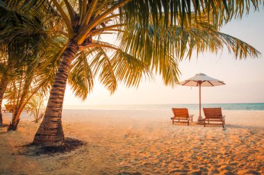 Beautiful tropical sunset scenery, two sun beds, loungers, umbrella under palm tree. White sand, sea view with horizon, colorful twilight sky, calmness and relaxation. Inspirational beach resort hotel. Summer holiday and vacation concept for tourism