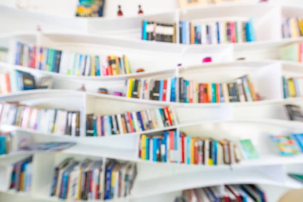 Blurred image of many books on curvy bookshelf in library background. Abstract blurred bookshelves with books, manuals and textbooks on bookshelves in library or in book store, for backdrop. Concept for education