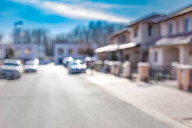 Modern lüks semtin bulanık sokak manzarası, evler arabalar ve güneşli mavi gökyüzü 