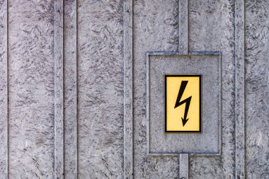 Gri metal bir yüzeyde yüksek voltaj belirtisi var. Yüksek voltaj belirtisi, gri bir metal yapıya vidalanmış..