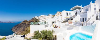 Oia ve Fira şehirleri, Yunanistan 'ın Santorini adası: Panoramik manzara, Caldera, Ege denizi üzerinde mavi kubbeleri olan geleneksel beyaz mimari ve ünlü beyaz evler ve kiliseler üzerinde güneşli gökyüzü. Lüks yaz tatili, romantik tatil.